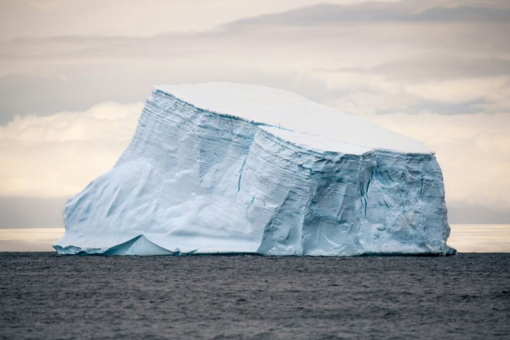 Iceberg flotando en el océano Atlántico bajo un cielo gris. Su tamaño es imponente sobre aguas oscuras.